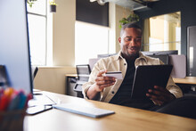 Smiling Man Making Online Payment On Tablet Computer Holding Credit Card In Office