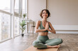 © Look! - Pretty young brunette woman practicing yoga at home . Caucasian cute girl looking away and smiling wearing green sportswear sitting on the floor. Concept of leisure, relaxation, workout
