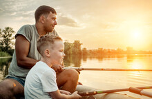Happy Father And Son Together Fishing From A Boat At Sunset Time, Summer Day, Beautiful Sky On Lake.
