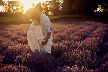 Wall Mural - young beautiful pregnant couple walking on a lavender field at sunset. Happy family concept