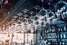 Wine Glasses Hanging And Drying In Bar Of Nightclub Or Restaurant With Dark Interior. Alcohol Cocktail Concept