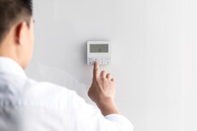 Close-up Photo. The Hand Of A Young Man In A White Shirt Turns On The Control Buttons Of The Air Conditioner Hanging On The Wall. Standing On The Left