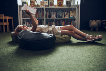 Wall Mural - Schoolgirl reading book in school library. Primary school pupil is involved in book. Child doing homework. Smart girl learning from book. Benefits of everyday reading