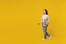 Full Body Side View Young Happy Smiling Woman She 30s Wears Striped Shirt White T-shirt Hold Use Closed Laptop Pc Computer Walk Go Isolated On Plain Yellow Background Studio. People Lifestyle Concept.
