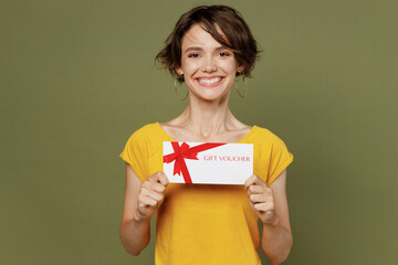 Wall Mural - Young smiling cheerful fun happy woman she 20s wear yellow t-shirt hold gift certificate coupon voucher card for store isolated on plain olive green khaki background studio. People lifestyle concept.