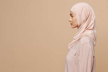 Sticker - Side view young arabian asian muslim woman 30s she wearing abaya hijab pink clothes isolated on plain pastel light beige background studio portrait. People uae middle eastern islam religious concept.