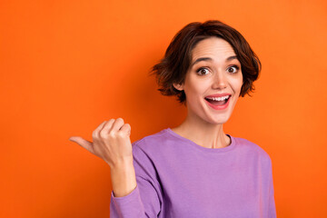 Poster - Photo of excited funny girl dressed purple pullover pointing thumb back empty space isolated orange color background