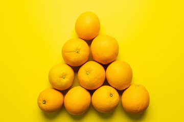 Wall Mural - Flat lay with oranges in triangle shape on yellow background.