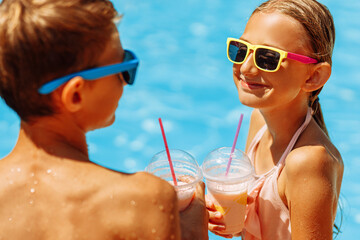 Child with drink in the outdoor pool. Children swim in a tropical resort. Healthy exotic fruit refreshing drink for kids