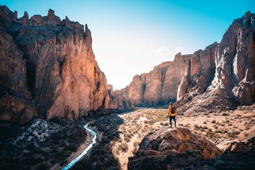 Wall Mural - Scenic view of a man standing on a stone against rock formations and a creek on a sunny day