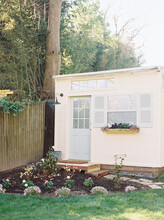 Small Ivory Shed With Blue Shutters And Garden