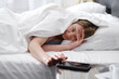 Sleepy Woman covered with blanket in the morning in bed turning off alarm clock On Cell Phone. Hard to wake up early from bed