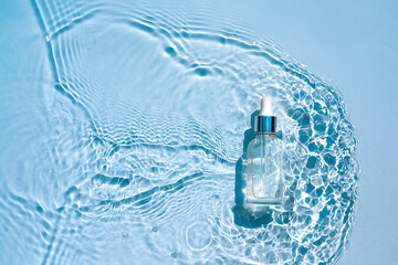 Wall Mural - Moisturizing cosmetic product, serum in a transparent bottle with a dropper in water waves, blue background