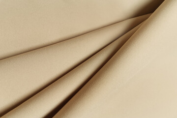 Beige crumpled or wavy fabric texture background. Abstract linen cloth soft waves. Gabardine wool fabric. Merino yarn. Smooth elegant luxury cloth texture. Concept for banner or advertisement.