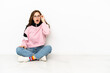 © luismolinero - Young caucasian woman sitting on the floor isolated on white background with glasses and surprised