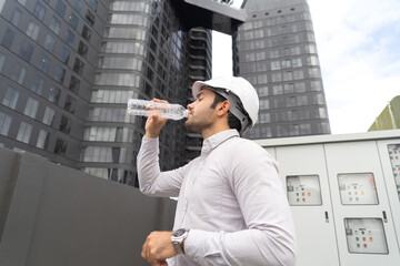 Wall Mural - A tired thirsty engineer man or worker, people working in industry factory, drinking water on rooftop building. System work machine. Water Supply pipe lines. Workshop site.