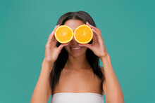 Joyful African American Girl Playing With Two Halves Of Orange, Covering Her Face Smiling On Turquoise Background, Copy Space