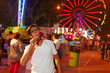 Happy Latino boy eating a caramelized apple at the fair with a Ferris wheel behind him.