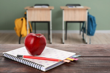 Notebook with pencil and apple on wooden table in classroom