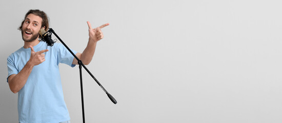 Wall Mural - Handsome young man singing in microphone and pointing at something on light background with space for text