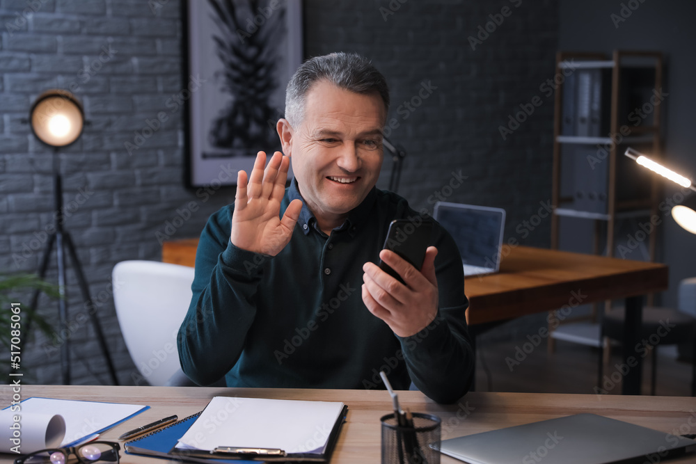 Happy mature man with mobile phone video chatting late in evening