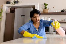 Low Angle View Of Biracial Mature Woman Wearing Gloves Cleaning Kitchen Island With Rag, Copy Space