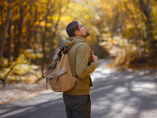 Wall Mural - Young handsome man posing in autumn forest. young hipster guy with backpack , traveller standing in woods, Hiking, Forest, Journey, active healthy lifestyle, adventure, vacation concept.