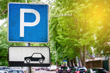 Wall Mural - Parking lot sign, cars parked under green trees in downtown, Parking zone. Parking problems not enough free space. Crowded public parking lot on narrow street. Rows of cars parked on roadside