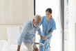 © amorn - Nurse and patient senior man. Female nurse caring old man using walker at hospital ward. Nurse helping elderly man using walker at nursing home.