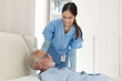 © amorn - Nurse taking care senior man to bed in the room at hospital. Asian female nurse caring elderly man patient in room at nursing home. Hospital care and older adults concept