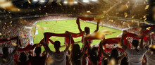 Back View Of Football, Soccer Fans Cheering Their Team With Colorful Scarfs At Crowded Stadium At Evening Time. Concept Of Sport, Support, Competition. Out Of Focus Effect