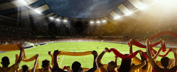 Wall Mural - Back view of football, soccer fans cheering their team with colorful scarfs at crowded stadium at evening time. Concept of sport, support, competition. Out of focus effect