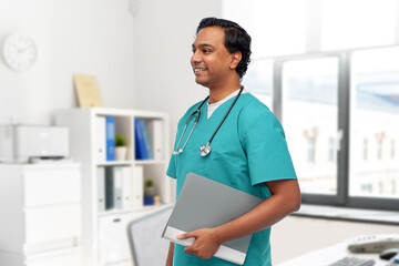 Wall Mural - healthcare, profession and medicine concept - happy smiling doctor or male nurse in blue uniform with folder and stethoscope over medical office at hospital on background