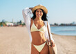 © Syda Productions - people, summer holidays and leisure concept - happy young woman in bikini swimsuit, white shirt and straw hat with bag walking along beach