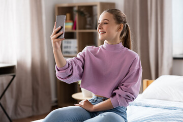 Wall Mural - people, children and technology concept - happy smiling teenage girl with smartphone taking selfie at home