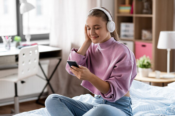 Wall Mural - technology and people concept - happy smiling girl in headphones with smartphone at home