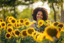 Woman Standing Behind A Lot Of Sunflowers, Smiling For The Camer