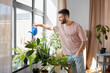 © Syda Productions - people, nature and plants care concept - happy smiling man watering flowers at home