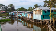 Puerto Narino, Colombia - Feb. 13, 2017: Beautiful Stilt Houses Built On Piles Over The Brown Water Of Amazon River. Favela Slums Of Local Indian Tribes. Poor Housing Protecting Against Flooding. 