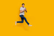 © deagreez - Full length photo of nice brunet millennial guy jump with telephone wear t-shirt jeans sneakers isolated on yellow background