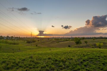 Wall Mural - The silhouette of electric poles the background of green hills, pastures and fields at sunset