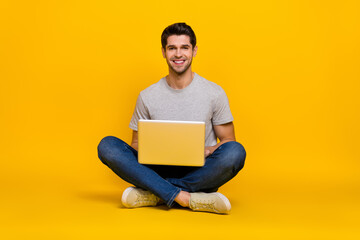 Portrait of attractive cheerful guy sitting using laptop writing email isolated over vibrant yellow color background