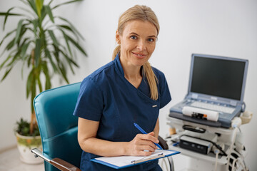 Wall Mural - Doctor ultrasound specialist makes notes in clipboard during patient appointment in clinic