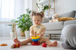 © Alla - Cute little girl playing with eco friendly toy. Toddler kid play with plastic free pyramid. Educational toys for preschool and kindergarten child. Girl build toy at home or daycare