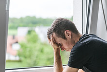 Young Sad Man Standing At The Window, Mentally Ill Teenager Looking Outside, Depression, Anxiety, Long Covid Symbol Image