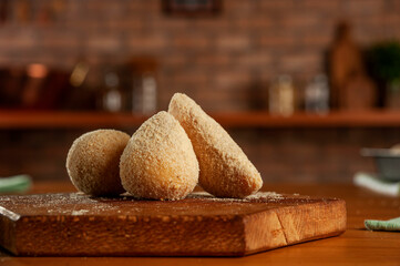 Breading brazilian croquettes (coxinha de frango, risolis de carne e bolinha de queijo) on kitchen bricks wall background.