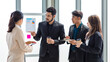 Group of millennial Asian Indian male female businessman businesswoman in formal suit standing holding tablet computer discussing sharing business ideas in multinational company office meeting room