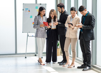 Group of millennial Asian Indian male female businessman businesswoman in formal suit standing holding tablet computer discussing sharing business ideas in multinational company office meeting room