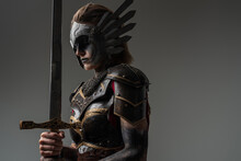 Shot Of Dramatic Female Warrior With Sword Dressed In Steel Armor Posing Agianst Grey Background.