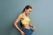 Fit young woman in lose jeans after losing weight isolated on blue background. Diet concept